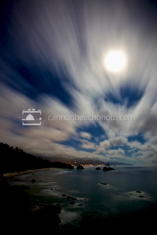 A slow exposure shows the motion of clouds over the Cannon Beach and the Pacific Ocean at night.